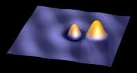 L'immagine tridimensionale in falso colore prodotta dal microscopio a scansione a effetto tunnel (STM) mostra due atomi d'oro sulla superficie isolante di una pellicola di NaCl. L'atomo a sinistra è stato intenzionalmente trasferito dal suo stato neutro a quello di ione negativo attraverso una manipolazione dell'STM