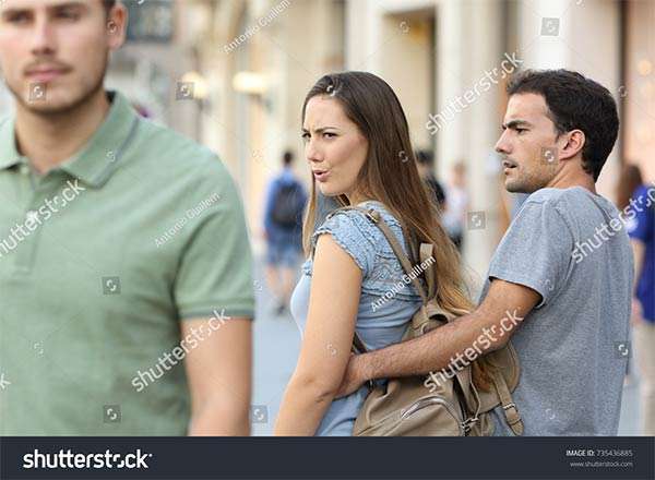 Disloyal woman looking another man and her angry boyfriend looking at her on the street